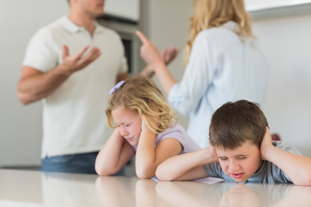 Niños cubriendo las orejas mientras los padres discuten