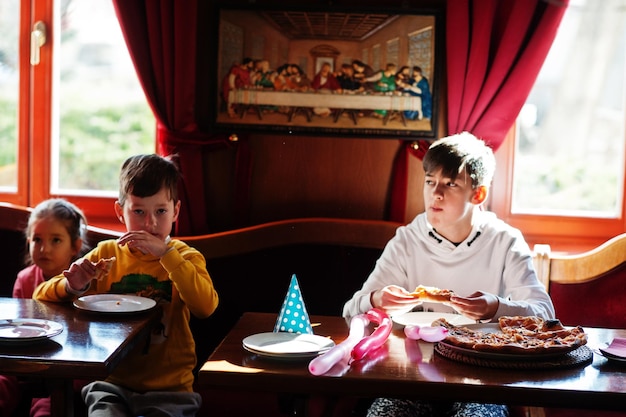 Niños en cumpleaños sentados en la mesa y comiendo pizza.