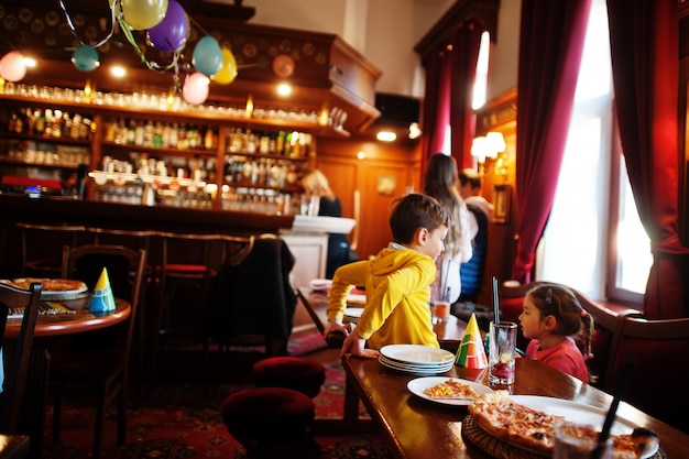 Niños en cumpleaños sentados en la mesa y comiendo pizza.