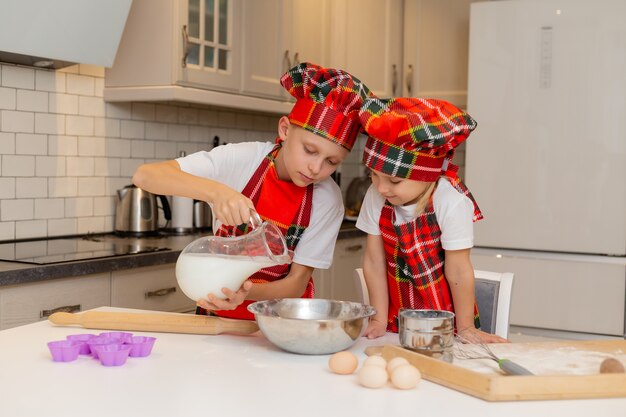 Los niños con disfraces de chef preparan masa de harina, leche, huevos y mantequilla para pasteles navideños.