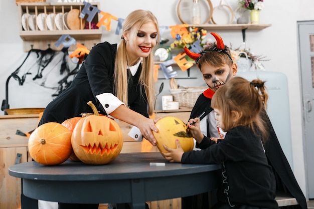 Los niños disfrazados de Halloween tallan ojos y bocas aterradoras en calabazas, la hermana mayor ayuda a los más pequeños. Foto de alta calidad