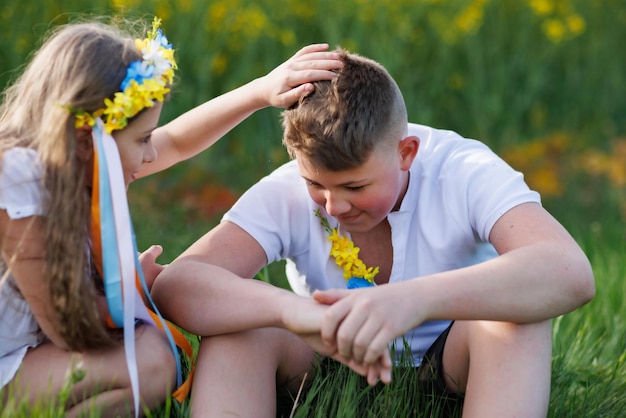 Los niños disfrutan del clima, hermano y hermana, se sientan en cuclillas y hablan en el campo con flores y hierba bajo el cielo