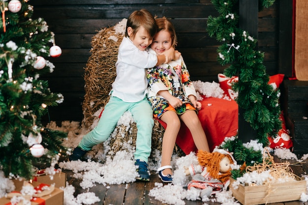 Niños divertidos abrazos en estudio con árbol de Navidad y decoraciones de año nuevo.