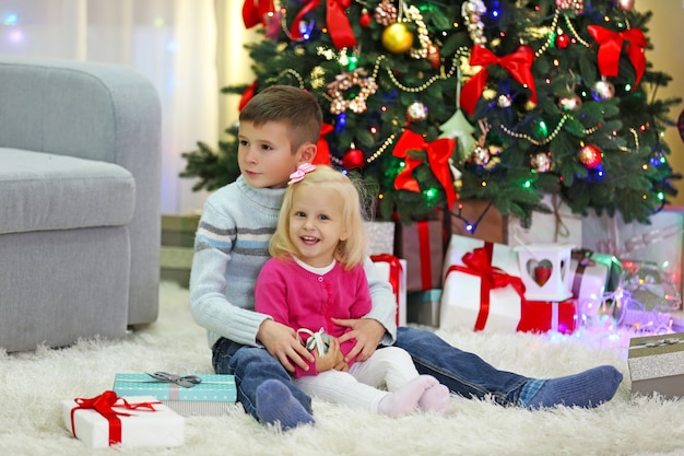 Niños divertidos con cajas de regalo y árbol de Navidad en el fondo