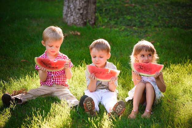 Niños divertidos comiendo sandía al aire libre en el parque de verano.