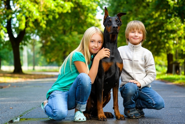 Niños con dobermann en el parque de verano.