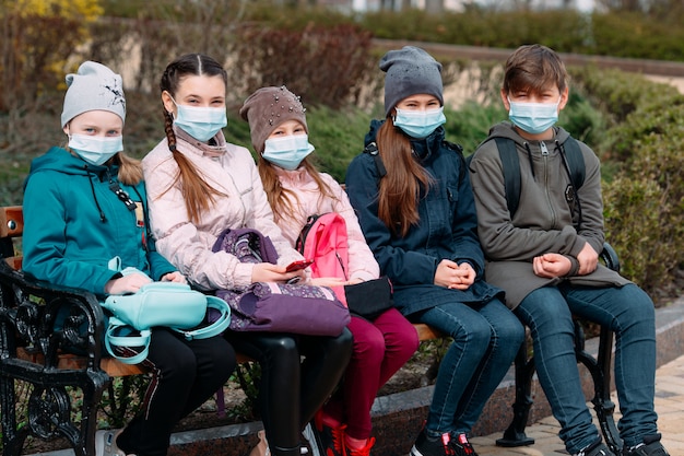 Los niños en edad escolar con máscaras médicas se sientan en un banco.