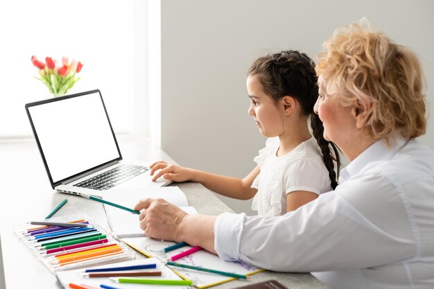 Niños y educación, maestra o abuela enseñando con cuaderno por internet a niña.