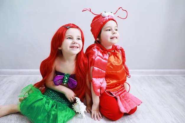 Niños en elegantes disfraces de carnaval sobre un fondo liso. Disfraz de criaturas de hadas marinas. Sirena y cangrejo. Hermano y hermana.