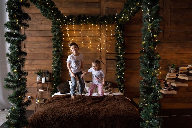 Niños emocionados saltando sobre la cama de los padres en casa como regalos familiares abiertos el día de Navidad