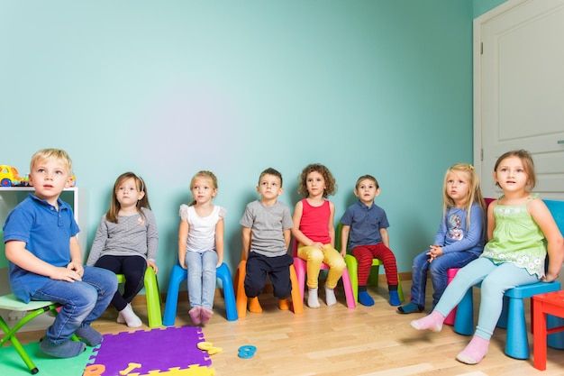Niños emocionados sentados en sillas escuchando al maestro con gran interés Preescolares comprometidos mientras lección interesante Sala con pared azul y piso de madera