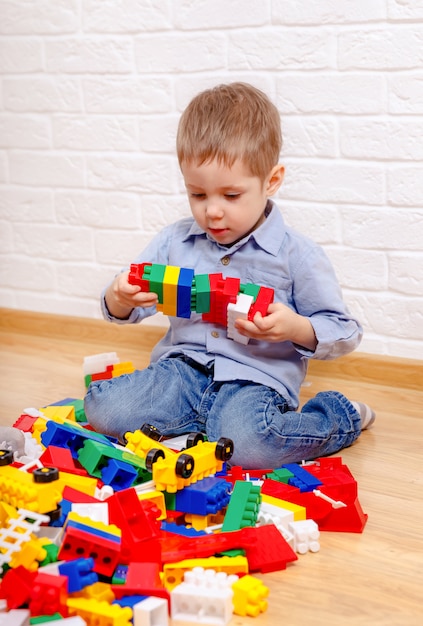 Niños encantadores jugando con constructor en piso en casa. Niños en edad preescolar divirtiéndose. Guardería, desarrollo infantil. Ladrillos de plástico de colores en el suelo.