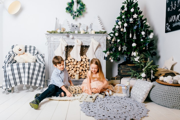 Niños encantadores jugando en la habitación con árbol de Navidad y chimenea. Concepto de vacaciones de invierno