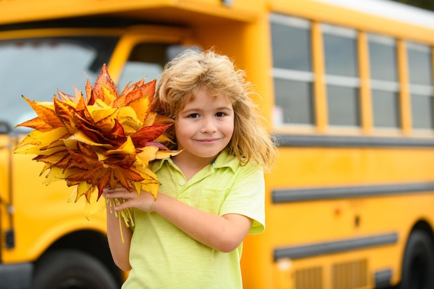 Los niños se enfrentan en otoño al aire libre de regreso a la escuela en septiembre otoño niño cerca del autobús escolar follaje de otoño sc