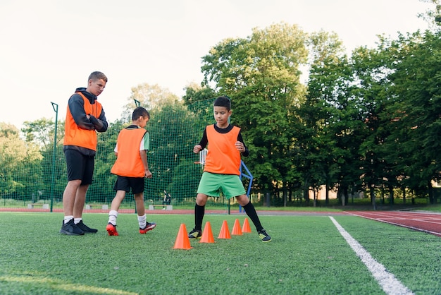 Niños entrenando entre conos de plástico durante los ejercicios de fútbol en el estadio.