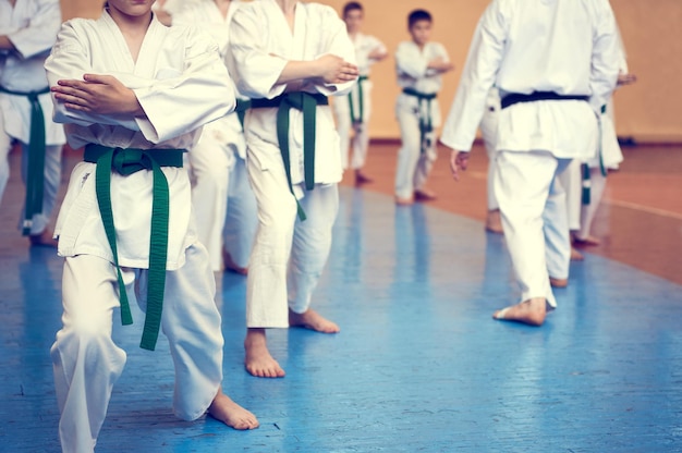 Niños entrenando en karatedo Atletas jóvenes en kimonos tradicionalmente blancos con cinturones de colores Banner con espacio para texto Estilo retro Para páginas web o impresión publicitaria Foto sin rostros