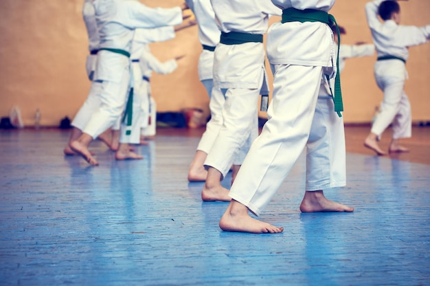 Niños entrenando en karatedo Atletas jóvenes en kimonos tradicionalmente blancos con cinturones de colores Banner con espacio para texto Estilo retro Para páginas web o impresión publicitaria Foto sin rostros