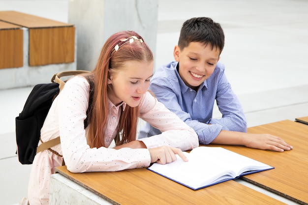 Niños, escolares, adolescentes leen en el patio de la escuela en un banco de madera. niño y niña son apasionados por el libro, el concepto de lectura