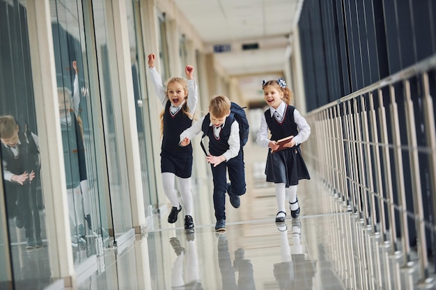 Niños de escuela activos en uniforme corriendo juntos en el corredor Concepción de la educación