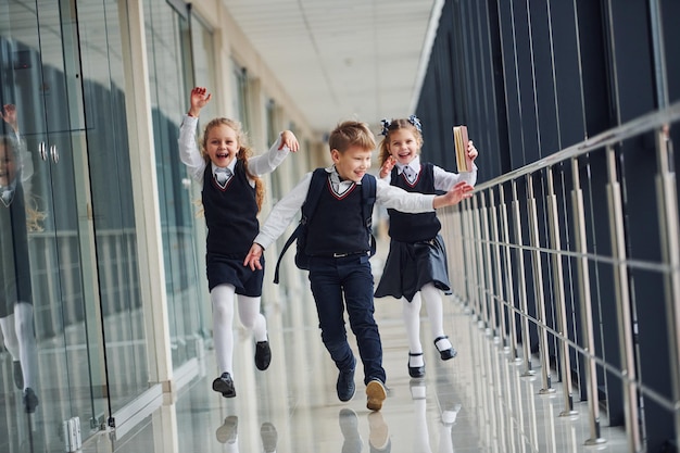 Niños de escuela activos en uniforme corriendo juntos en el corredor Concepción de la educación