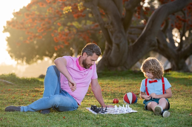 Niños de la escuela de ajedrez padre e hijo jugando al ajedrez tirado en la hierba en el parque de césped día del padre amor familia p ...