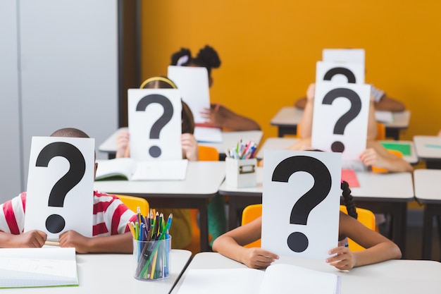 Niños de la escuela cubriendo su rostro con signo de interrogación