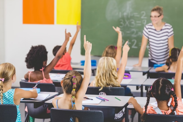 Niños de la escuela levantando la mano en el aula