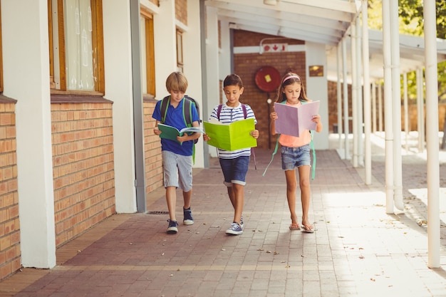 Niños de la escuela leyendo libros mientras camina en el pasillo