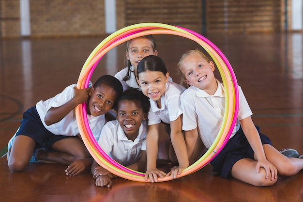 Niños de la escuela mirando a través del hula hoop en la cancha de baloncesto