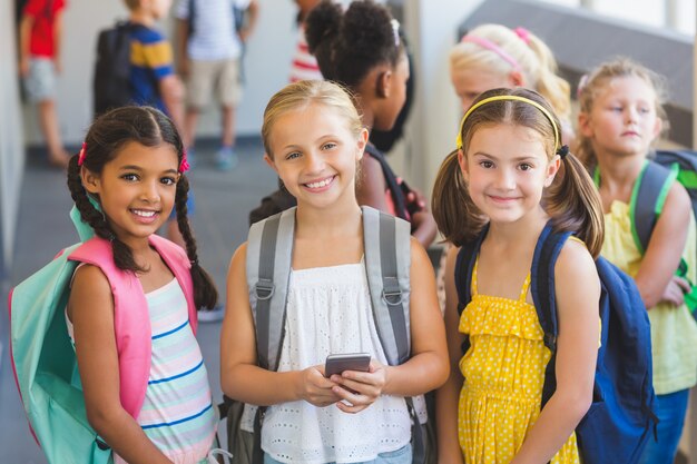 Niños de la escuela de pie en el pasillo con teléfono móvil