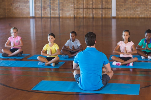 Niños de la escuela y profesor meditando durante la clase de yoga