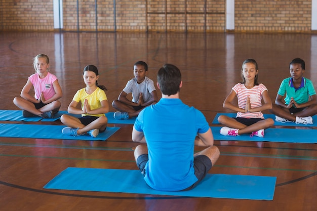 Niños de la escuela y profesor meditando durante la clase de yoga