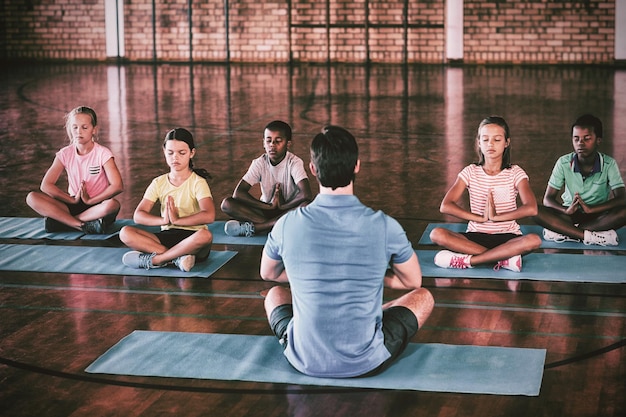 Niños de la escuela y profesor meditando durante la clase de yoga