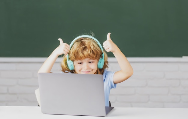 Niños de la escuela con los pulgares hacia arriba usando computadora portátil y auriculares en clase en la escuela