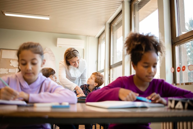 Los niños de la escuela que estudian en el aula con el maestro en segundo plano.