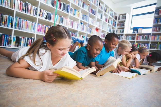 Niños de la escuela en suelo leyendo el libro en la biblioteca