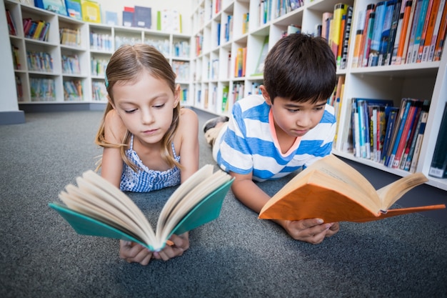 Niños de la escuela tirado en el piso y leyendo un libro en la biblioteca