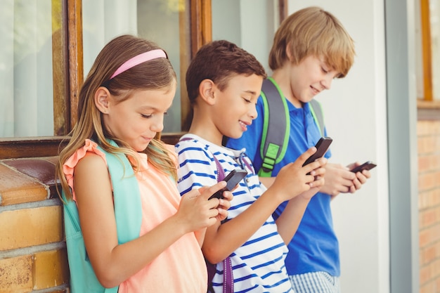 Foto niños de la escuela usando un teléfono móvil en el pasillo