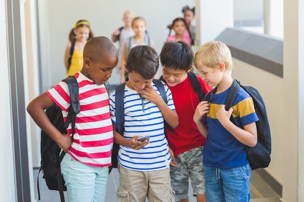 Niños de la escuela usando un teléfono móvil en el pasillo