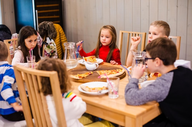 Los niños están comiendo una mesa de madera de pizza en el café.