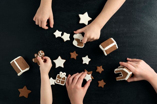 Los niños están jugando con galletas de jengibre de año nuevo. Vista superior sobre fondo negro.