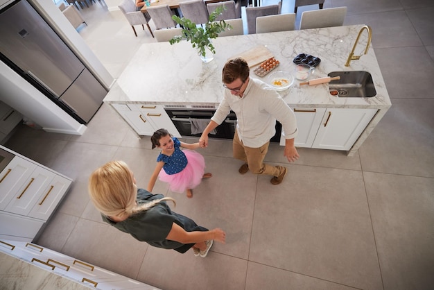 Los niños de la familia bailan con una niña y sus padres bailando juntos en la cocina de su casa. Sonríe divertido y juguetón con una niña, su madre y su padre se sienten felices en su casa.