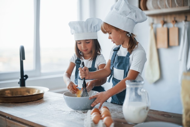 Niños de la familia en uniforme de chef blanco preparando la comida en la cocina.