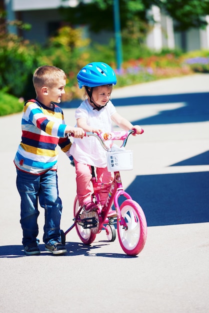 Niños felices al aire libre, hermano y hermana en el parque se divierten. Niño y niña en el parque aprendiendo a andar en bicicleta.