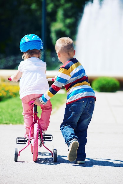 Niños felices al aire libre, hermano y hermana en el parque se divierten. Niño y niña en el parque aprendiendo a andar en bicicleta.