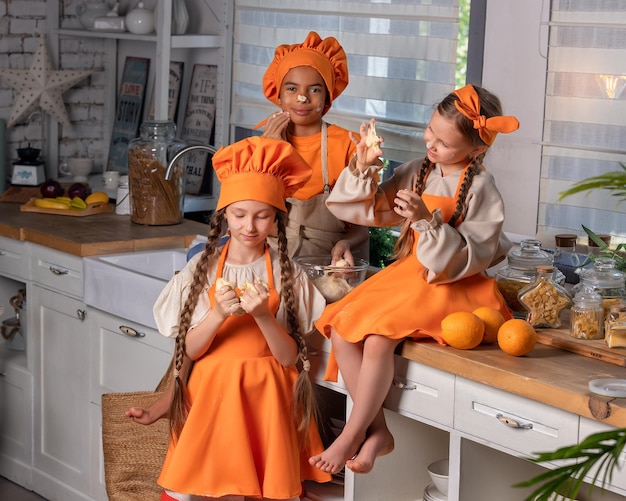 Niños felices amigos comiendo naranja fresca y jugando con frutas frescas de mandarina en la cocina en casa