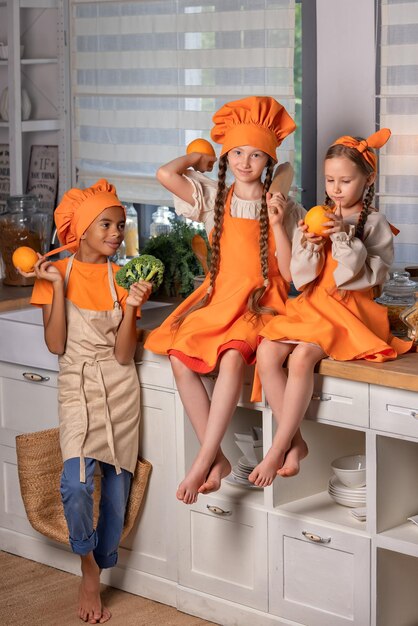 Niños felices amigos comiendo naranjas frescas y jugando con frutas frescas de mandarina en la cocina en casa Niños concepto de alimentación saludable Familia comunicando culinaria y disfrutando del fin de semana