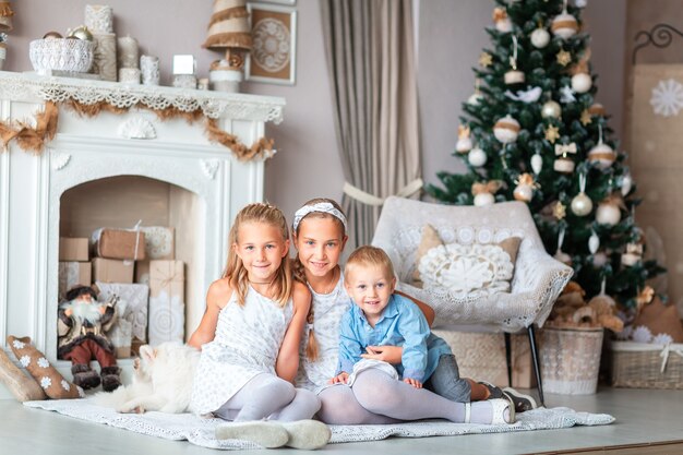 Niños felices cerca del árbol de Navidad con regalos junto a la chimenea