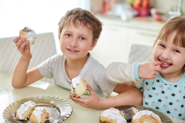 Foto niños felices comen pasteles en la luminosa cocina de la mesa