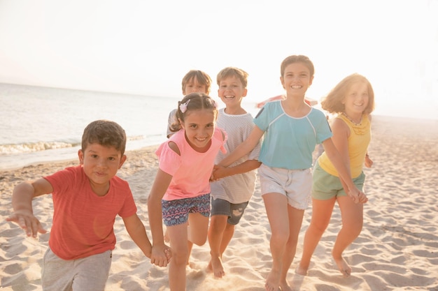 Niños felices corriendo en la playa al atardecer Niños alegres pasando un buen rato en las vacaciones de verano Niños y niñas sonrientes de vacaciones en la orilla del mar